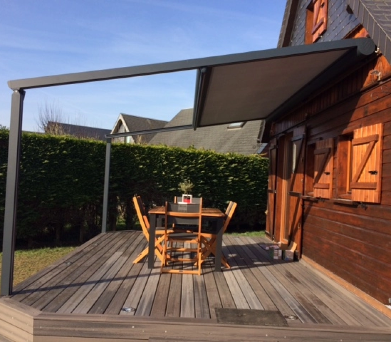 Store pergola gris anthracite sur terrasse bois, table et chaises devant chalet bois