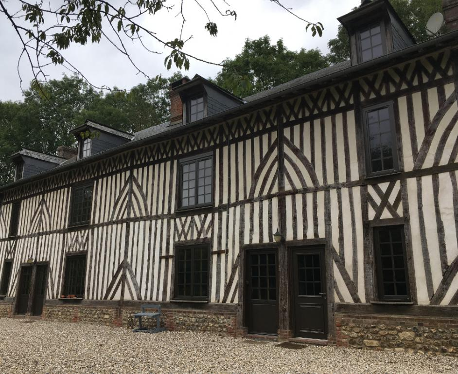 Longue maison colombages, nombreuses fenêtres sombres à petits carreaux, gravier devant