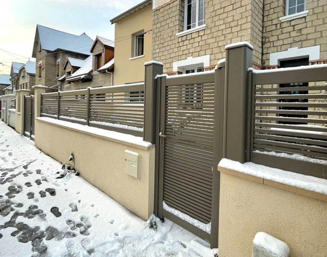 Cloture et portillon marron lames horizontales ajourées sur muret sous la neige