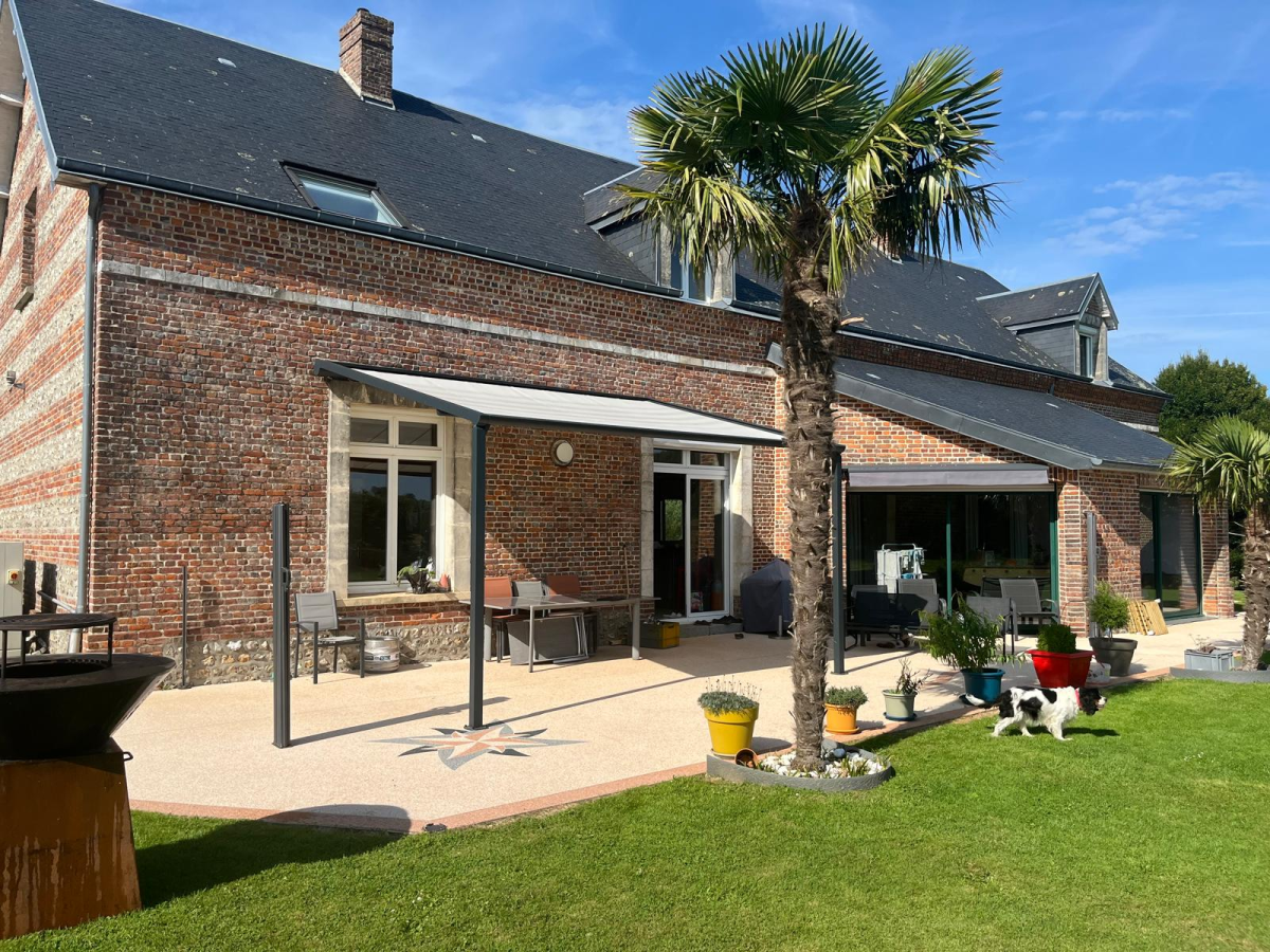 Pergola blanche et toile rouge rétractable sur terrasse bois, devant maison bardée gris clair