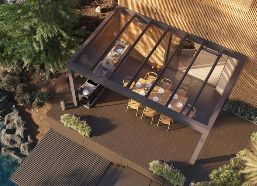 Pergola toit vitre anthracite sur terrasse bois avec table, cuisine exterieure et pins