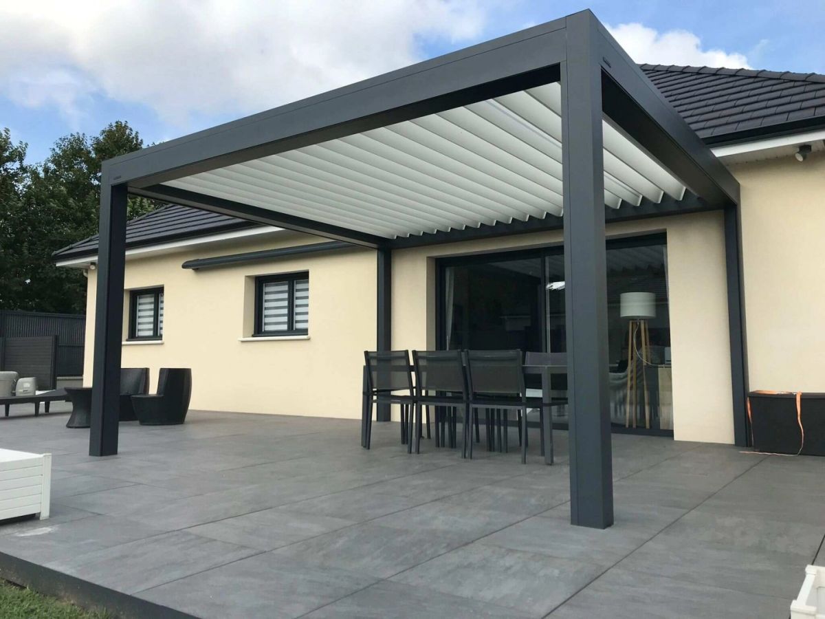 Pergola bioclimatique gris a lames blanches sur terrasse carrelée avec table et chaises