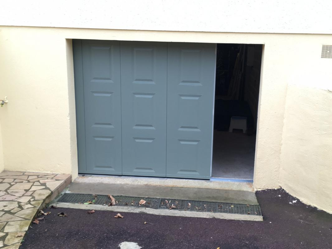 Porte garage latérale gris vert, quatre vantaux moulurés, un panneau coulissant ouvert