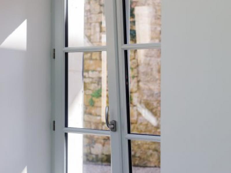 Détail poignée alu sur fenêtre blanche à petits carreaux, mur intérieur blanc