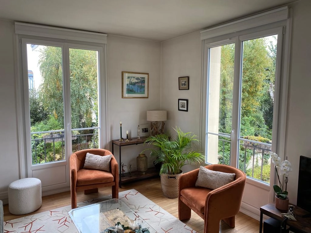 Deux portes-fenêtres blanches, fauteuils velours terracotta, console et jardin dense