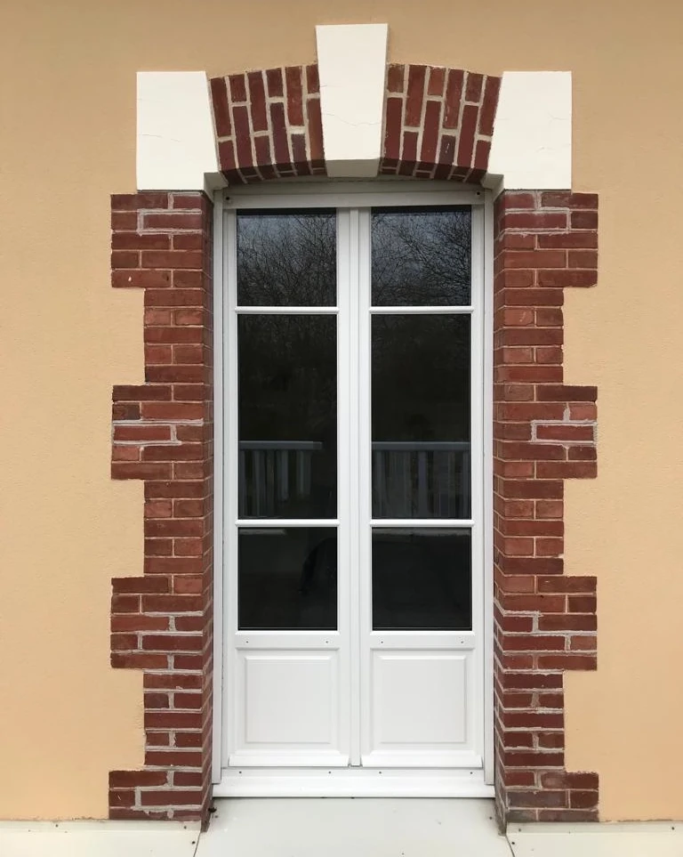 Porte-fenêtre double blanche petits carreaux, encadrement briques rouges et arc en brique