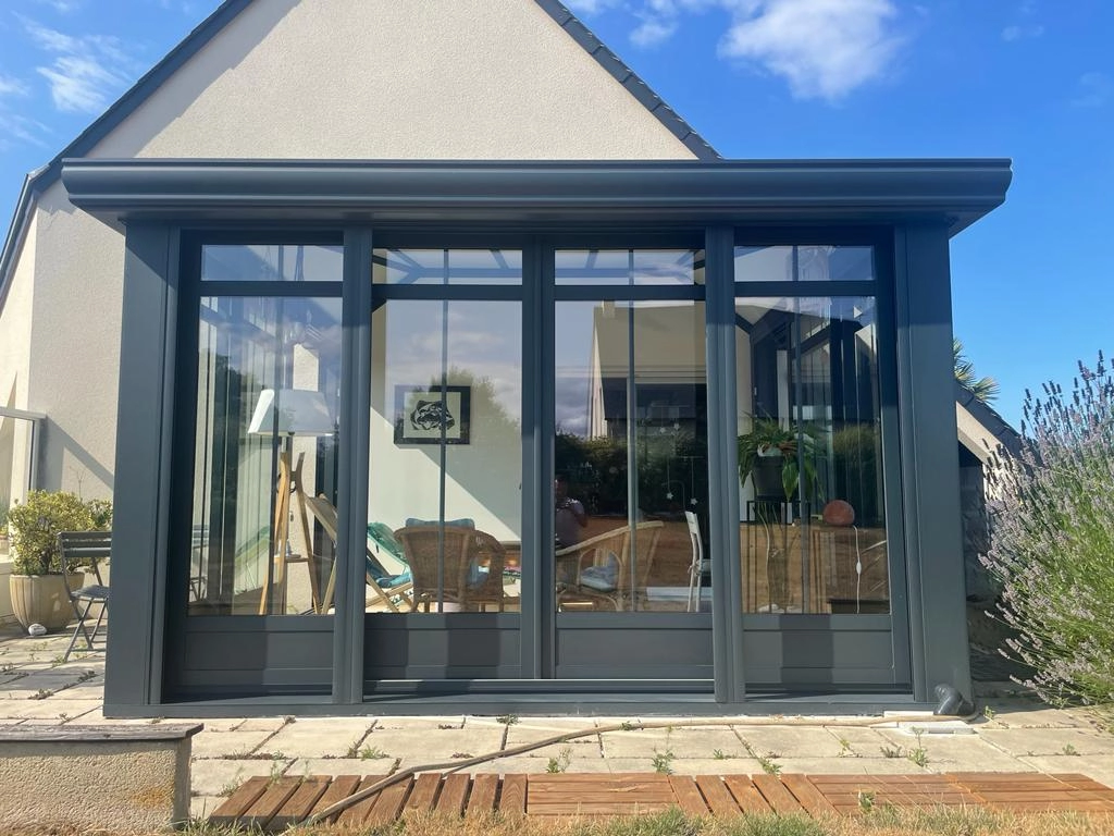 Véranda gris anthracite baies vitrées, salon osier visible, terrasse pavée et lavande