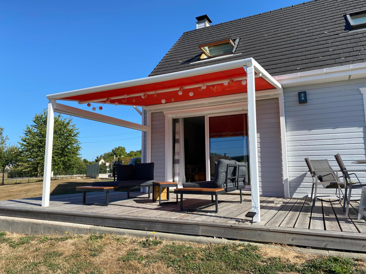 Pergola blanche toiture rouge, salon noir sur terrasse bois, guirlandes et jardin vert