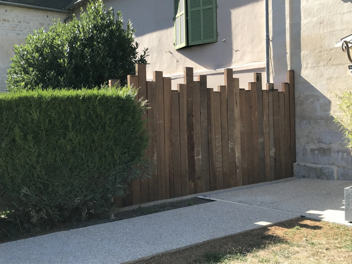 Cloture decorative planches bois verticales hauteurs décalées devant haie et facade
