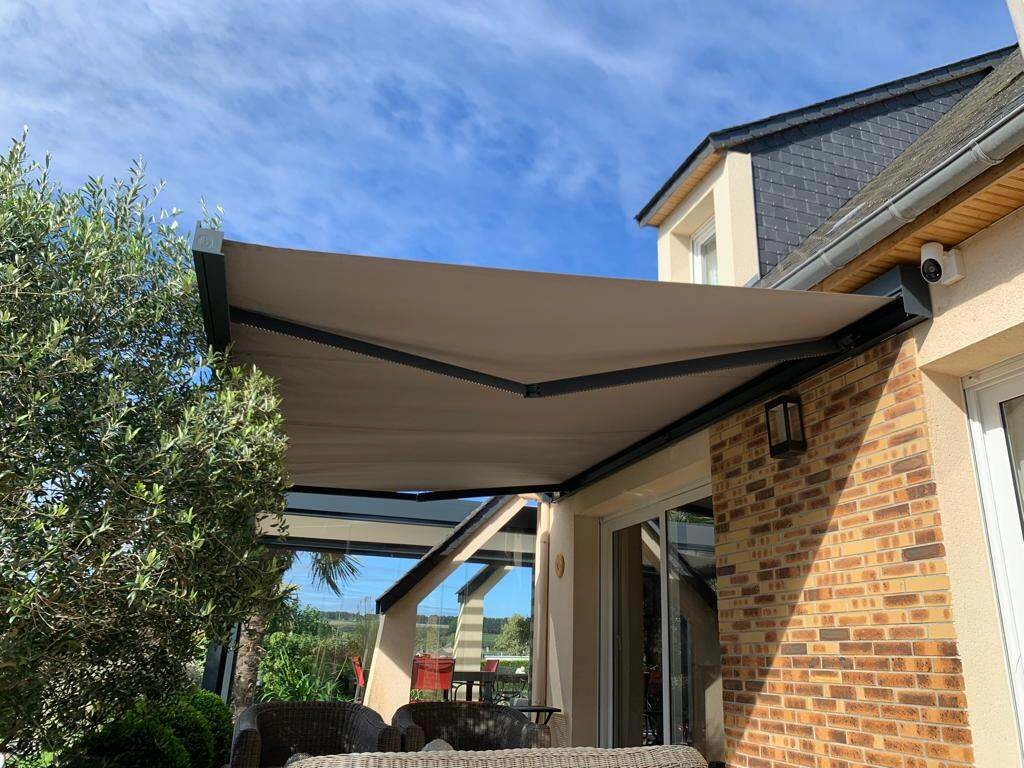 Store banne beige déployé, armature anthracite, façade briques, ciel bleu ensoleillé