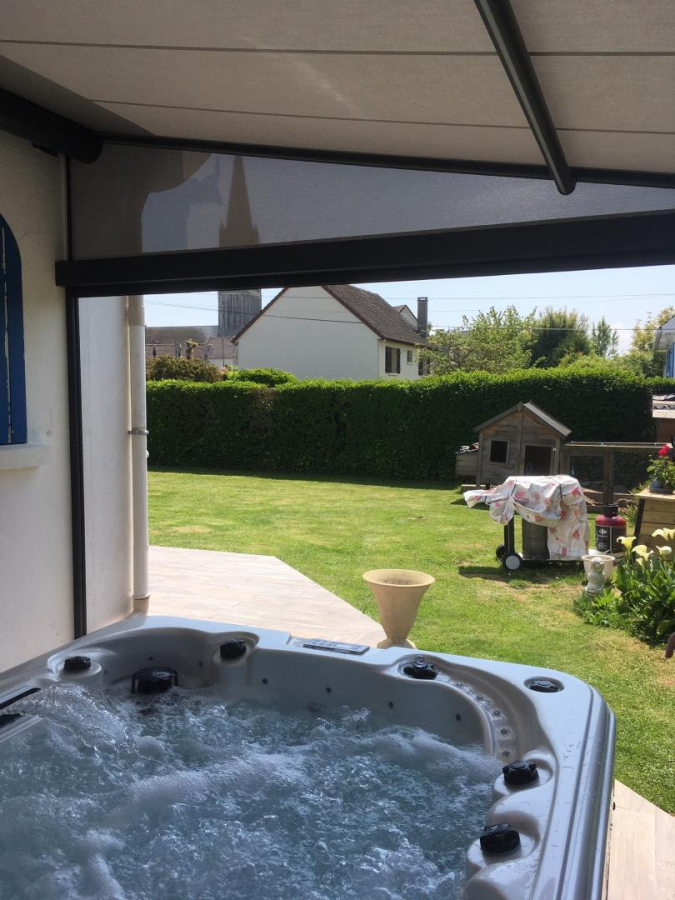 Spa blanc sous pergola toile beige et store latéral noir, vue jardin clôturé