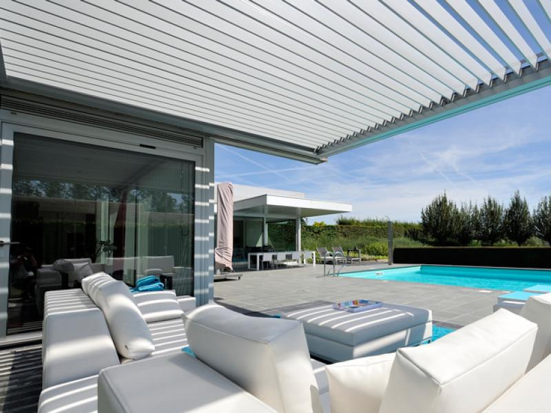 Pergola bioclimatique blanche à lames orientables, salon blanc et piscine turquoise