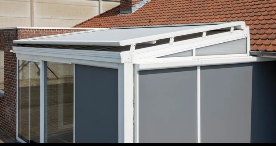Véranda blanche, store toiture gris, stores verticaux gris baissés, murs briques rouges