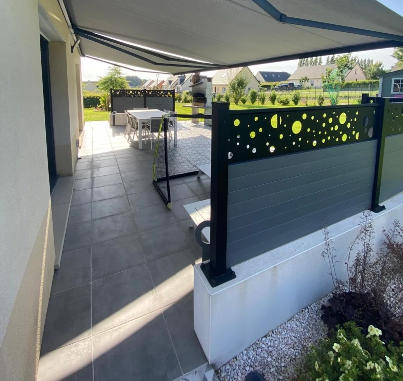 Terrasse dalles grises, store banne anthracite, brise-vue perforé bulles, salon de jardin
