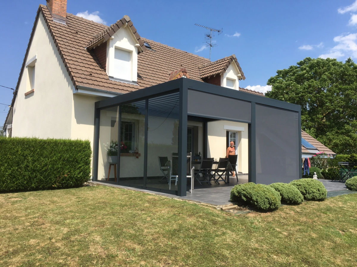 Veranda anthracite stores lateraux gris, table et chaises sur terrasse carrelée