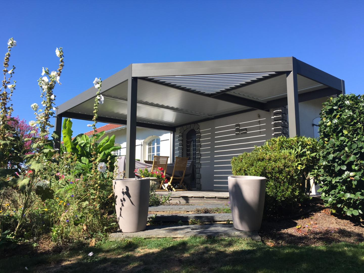 Pergola bioclimatique gris anthracite, lames orientables blanches sur terrasse fleurie