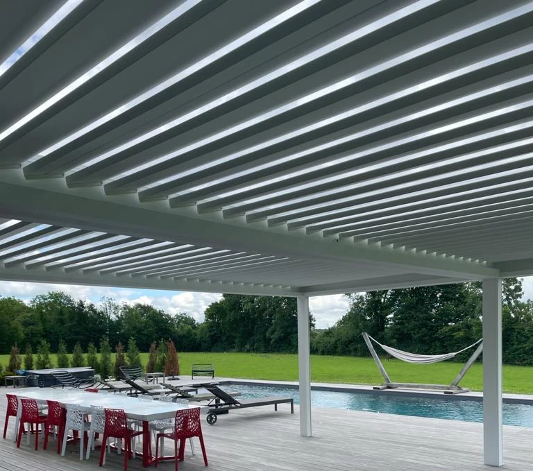 Pergola bioclimatique blanche sur terrasse avec piscine, table blanche et transats