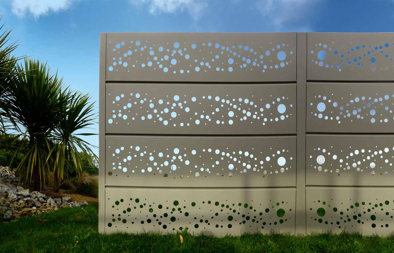 Cloture gris clair a lames horizontales perforees motif bulles sur pelouse et ciel bleu