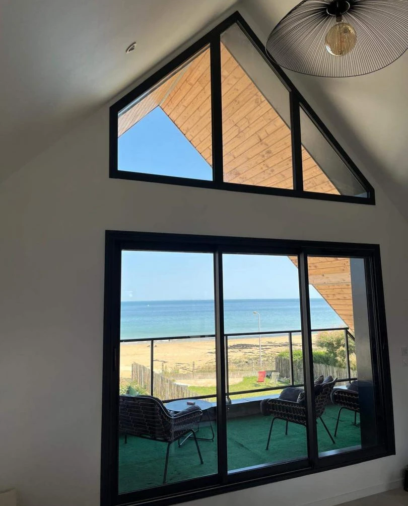 Baie vitrée noire et imposte triangulaire, balcon gazon synthétique et vue mer