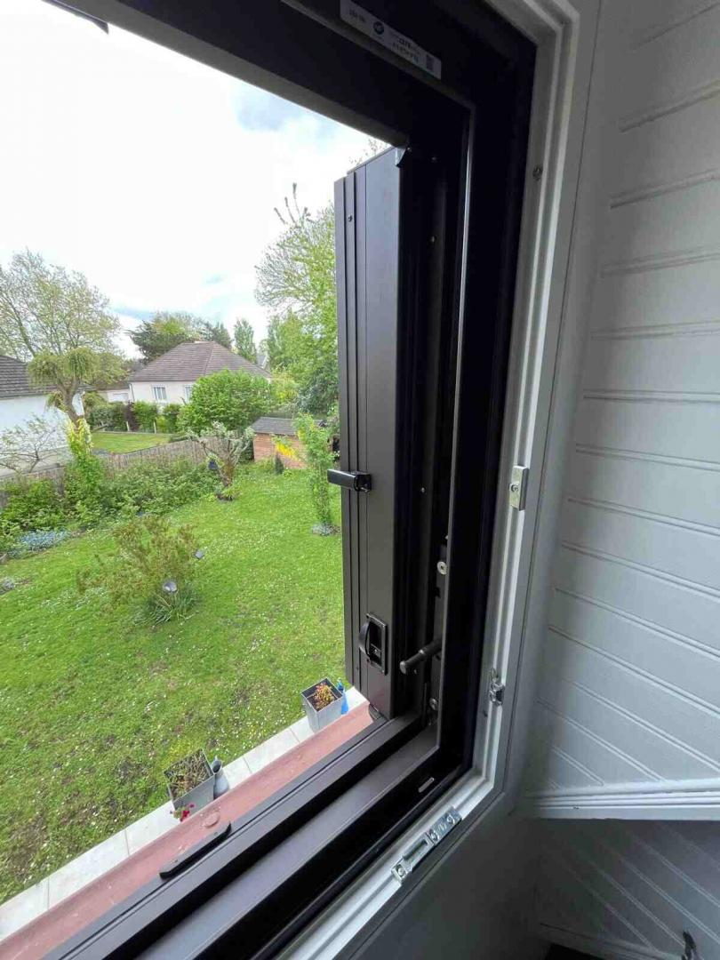Fenêtre ouverte, volet pliant marron intégré, vue jardin vert depuis pièce blanche