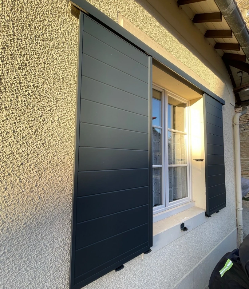 Volets coulissants anthracite à lames, fenêtre blanche petits bois, façade crépi beige