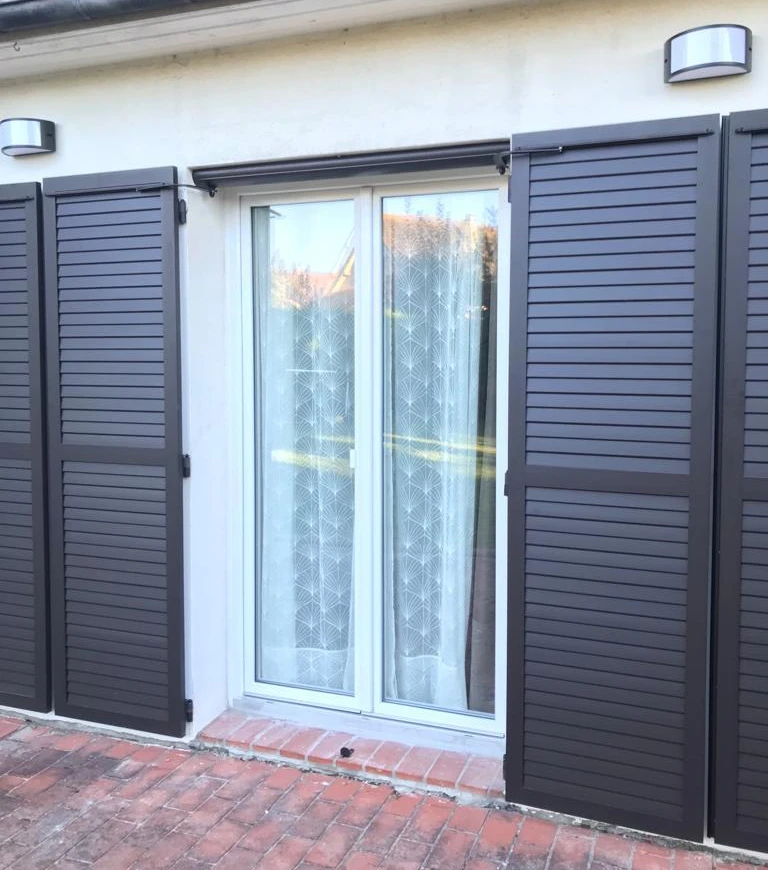 Porte-fenêtre blanche, volets coulissants anthracite à lames, crépi beige, applique