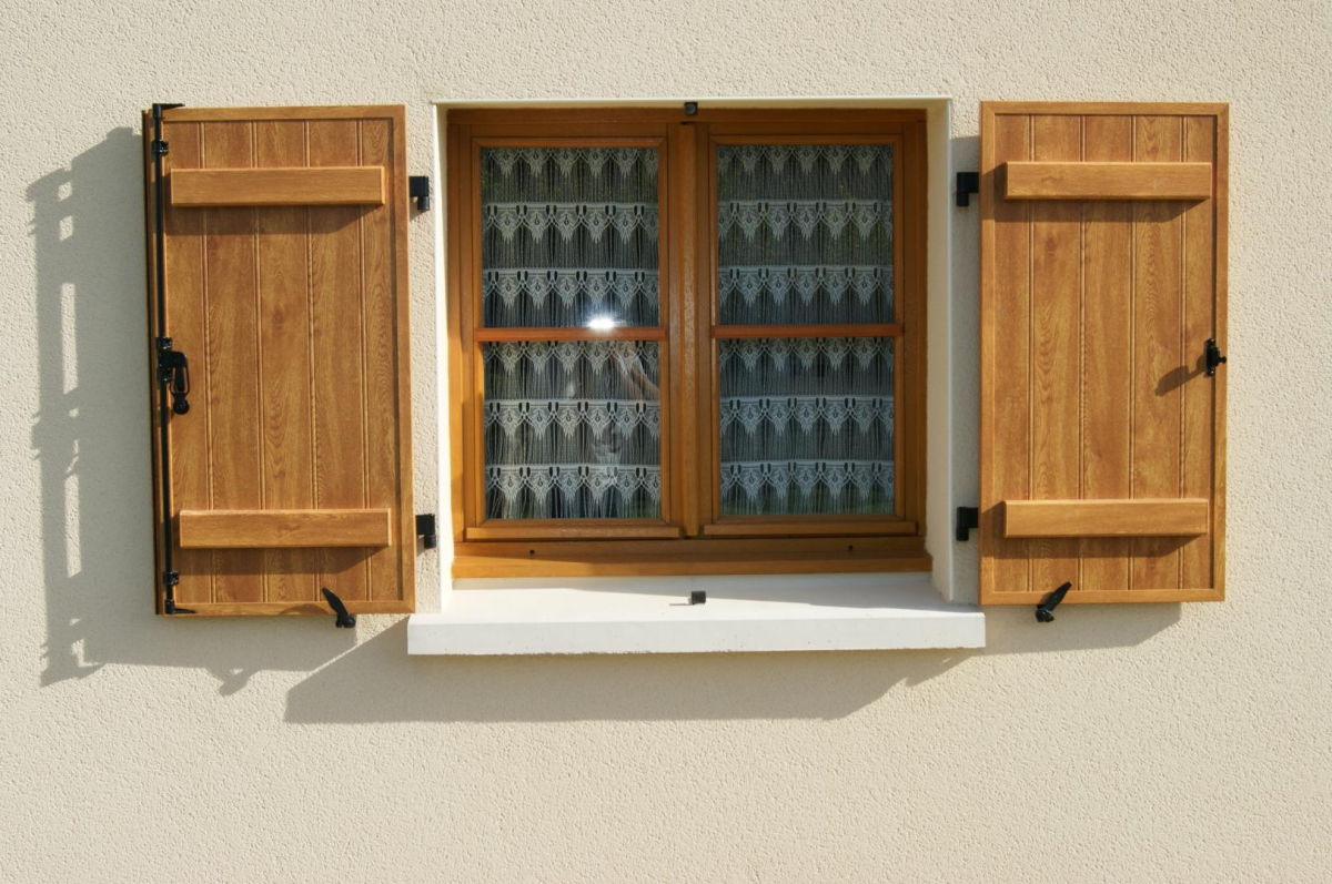 Fenêtre bois, volets battants chêne clair ouverts, rideaux dentelle blanche, crépi beige