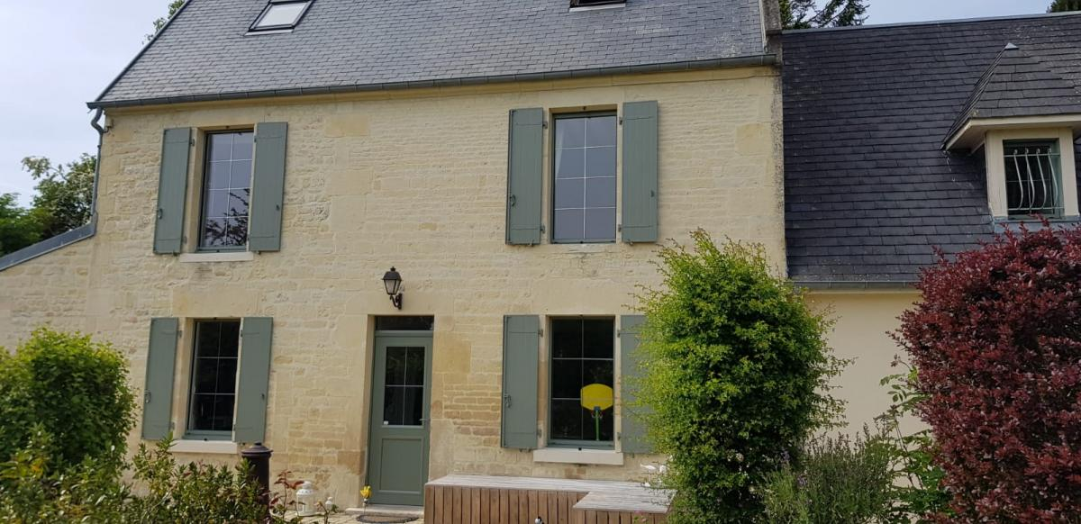 Maison pierre, volets battants vert sauge, porte assortie, toit ardoise et arbustes