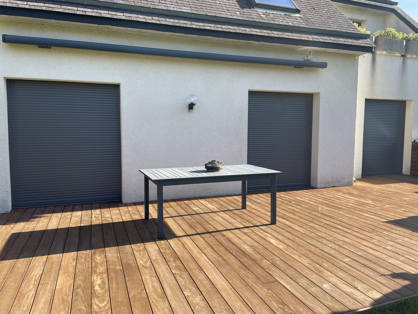 Terrasse bois, trois volets roulants anthracite fermés, coffre store banne gris au-dessus