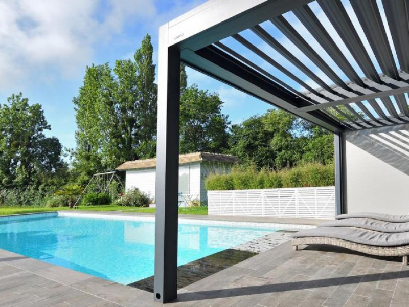Pergola bioclimatique anthracite au bord d'une piscine avec chaises longues