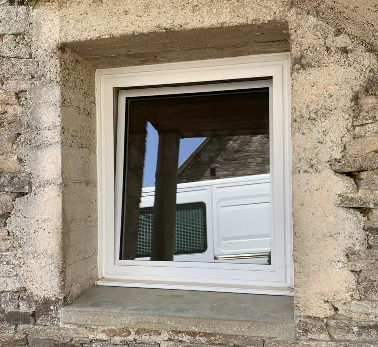 Fenêtre blanche oscillo-battante entrouverte, posée en rénovation sur mur en pierres