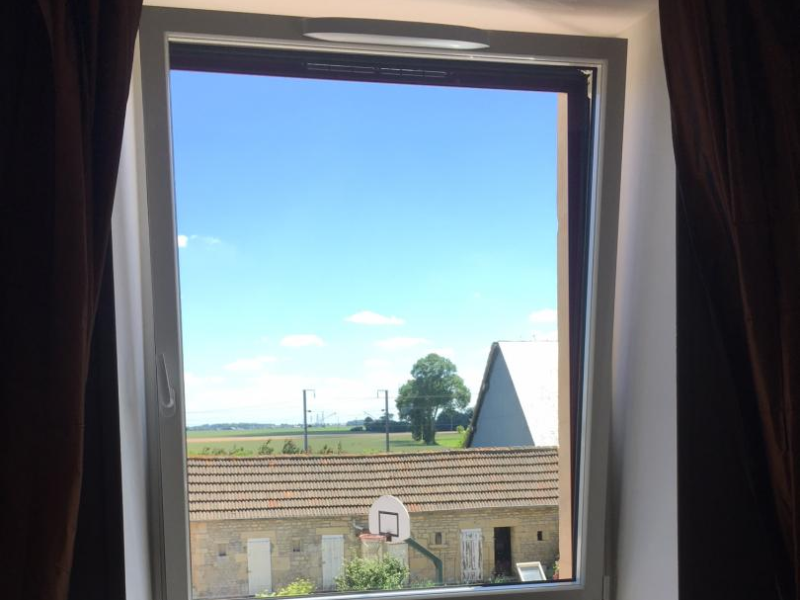 Fenêtre PVC blanche oscillo-battante avec rideaux bruns et radiateur, vue campagne