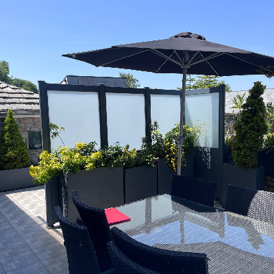 Terrasse extérieure avec panneaux brise-vue en verre dépoli, jardinières anthracite, parasol noir et salon de jardin