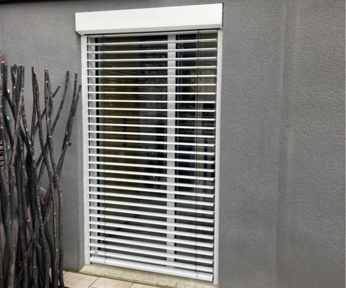 BSO blanc incliné sur porte vitrée, mur gris texturé, dalles beige et ardoises en toit