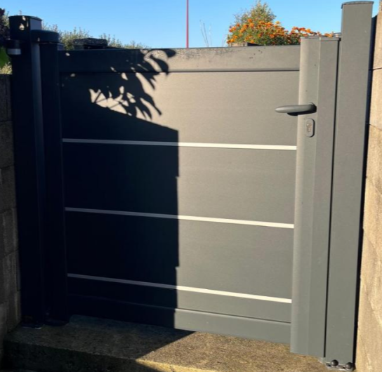 Portillon anthracite lames horizontales au sommet de marches pierre sous ciel bleu