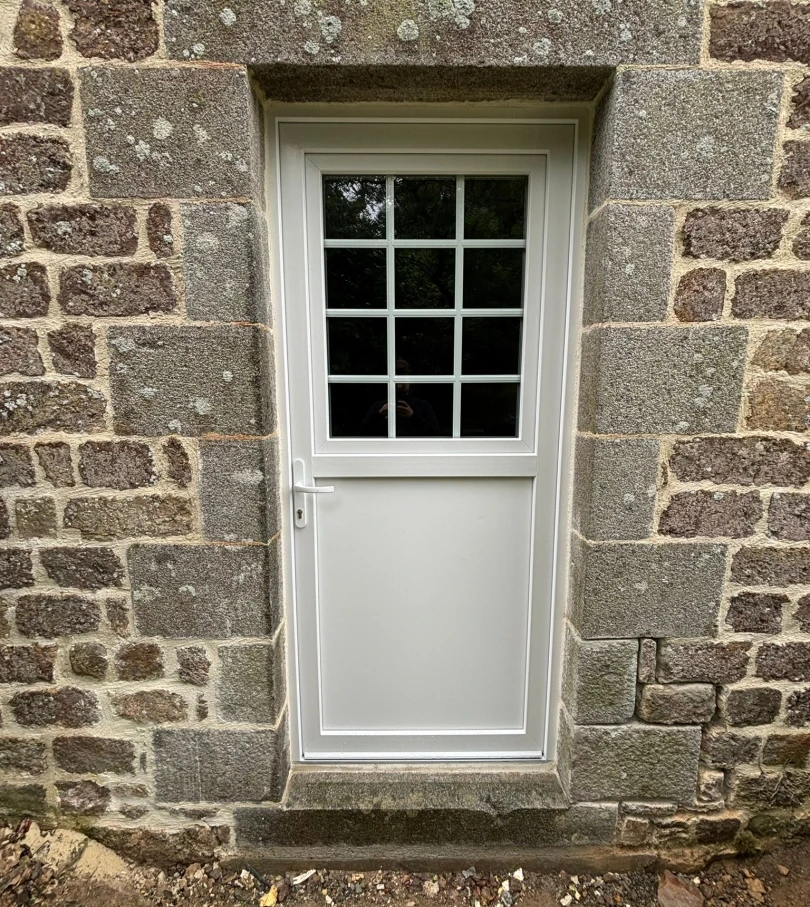 Porte PVC blanche, imposte à petits bois, panneau bas plein, mur pierre apparente