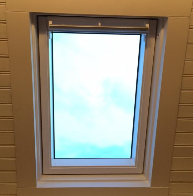 Fenêtre de toit blanche dans lambris blanc, ciel nuageux bleu et gris
