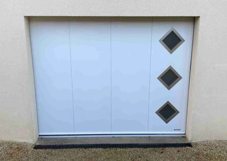 Porte garage latérale blanche, trois hublots losange à droite, applique ronde, gravier
