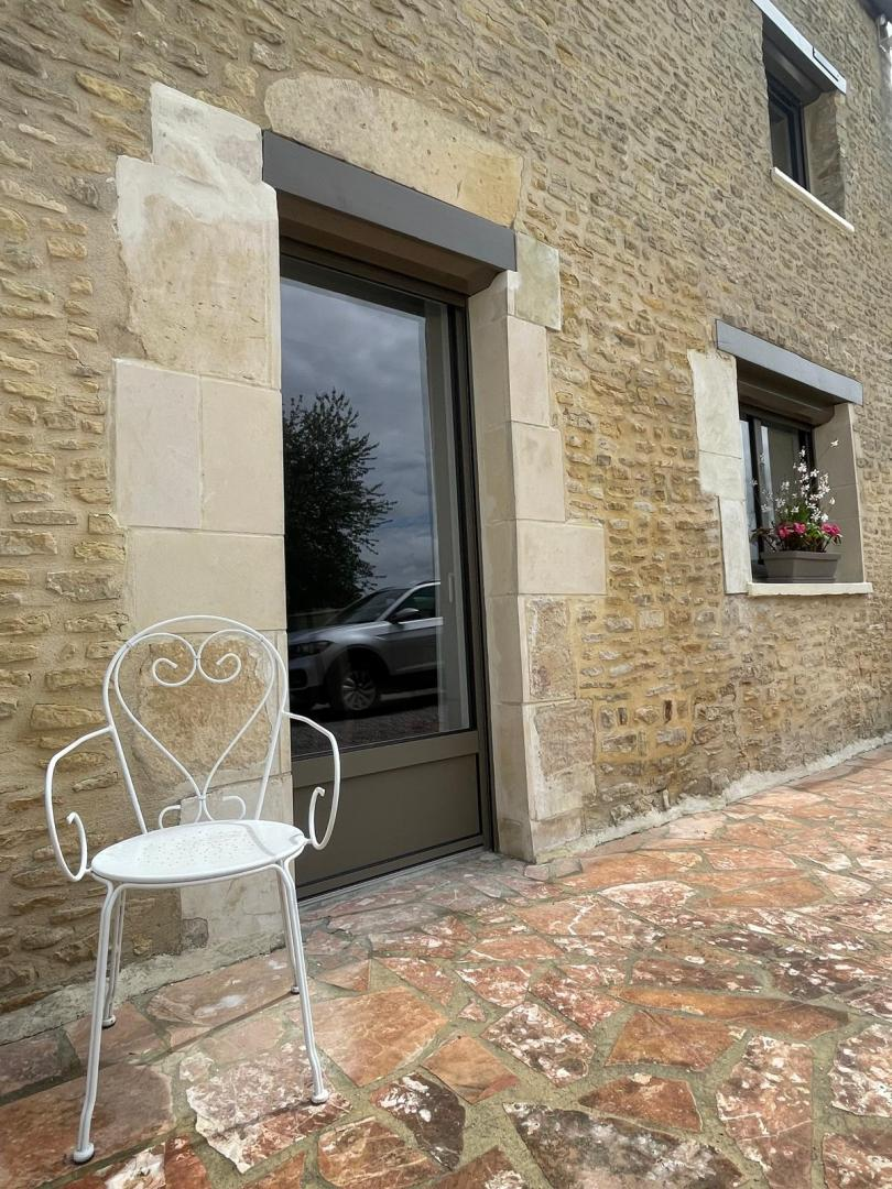 Porte-fenêtre à cadre brun foncé dans une façade en pierres, terrasse dallée et jardinière