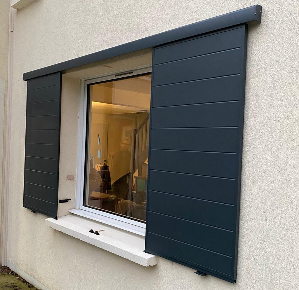 Paire de volets coulissants alu anthracite à lames sur fenêtre blanche, façade crépi clair