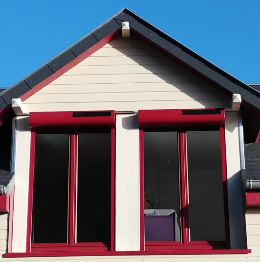 Lucarne deux fenêtres rouge bordeaux, volets roulants solaires, bardage clair, ciel bleu
