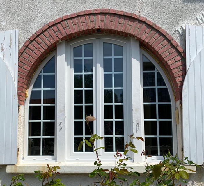 Fenetre cintrée blanche a petits bois sous arche en briques rouges et volets ouverts