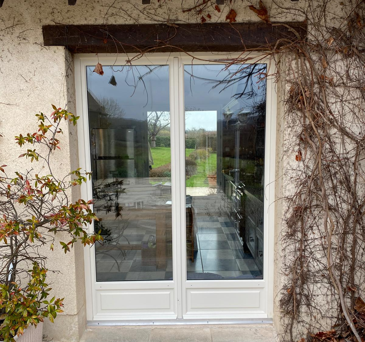 Porte-fenêtre blanche double battant avec soubassements, façade pierre et linteau bois
