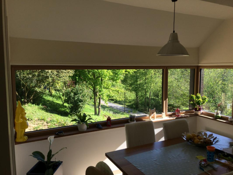Fenêtre d'angle en bois clair avec vue sur jardin, table et chaises blanches
