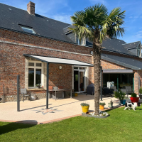 Pergola adossée anthracite, toiture toile claire sur terrasse carrelée devant maison en briques