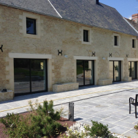 Longère en pierre avec quatre baies coulissantes alu noires au rez-de-chaussée et terrasse pavée claire