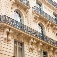 Fenêtres blanches cintrées et balcon fer forgé sur immeuble pierre beige à bossages horizontaux