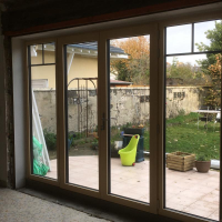 Baie vitrée blanche quatre vantaux avec petits bois, vue jardin depuis pièce en travaux