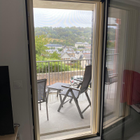 Moustiquaire fine sur porte-fenêtre balcon, chaises pliantes grises et vue collines verdoyantes
