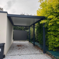 Carport adossé gris anthracite toiture blanche, deux poteaux sur allée gravier devant clôture lames